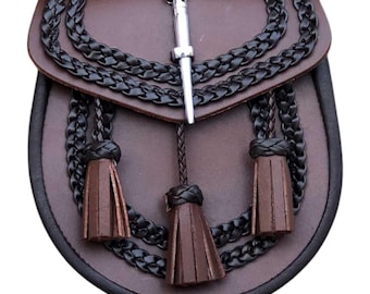 Könnte beinhalten: Eine braune Leder-Sporran mit schwarzem geflochtenem Besatz und drei braunen Quasten. Die Sporran hat einen silbernen Metall-Cantle und einen Kettenverschluss. Traditionelles schottisches Accessoire.