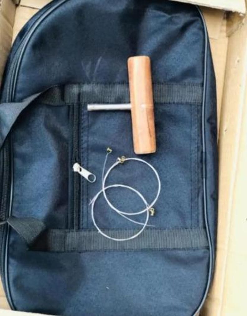 May include: A black nylon guitar case with a zipper, a wooden tuning tool, and two guitar strings. The case has a pocket with a zipper. The tuning tool is brown and cylindrical.