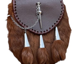 May include: A brown leather sporran with a fur body and silver accents. The sporran features a flap top with decorative stitching, a silver chain, and three silver cone-shaped tassels. The fur is a rich, dark brown color.