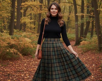 May include: A person in a black turtleneck and a green and brown plaid skirt stands in a forest. They wear black boots and carry a brown handbag. The ground is covered in fallen leaves, and the trees have yellow and brown leaves.