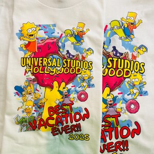 May include: Two white t-shirts with a colorful graphic featuring characters from The Simpsons. The design includes the text "UNIVERSAL STUDIOS HOLLYWOOD" and "BEST VACATION EVER!! 2025" with images of Bart Simpson skateboarding and donuts.