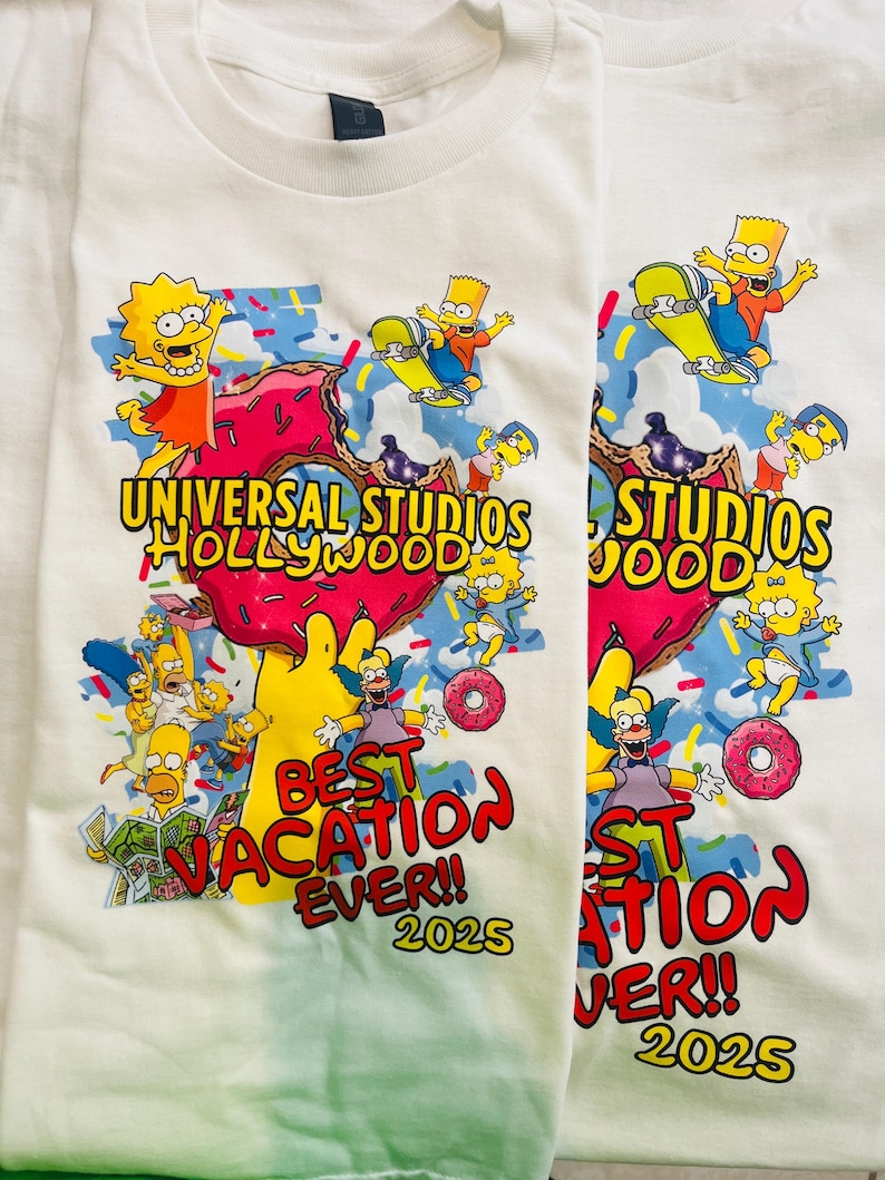 May include: Two white t-shirts with a colorful graphic featuring characters from The Simpsons. The design includes the text "UNIVERSAL STUDIOS HOLLYWOOD" and "BEST VACATION EVER!! 2025" with images of Bart Simpson skateboarding and donuts.