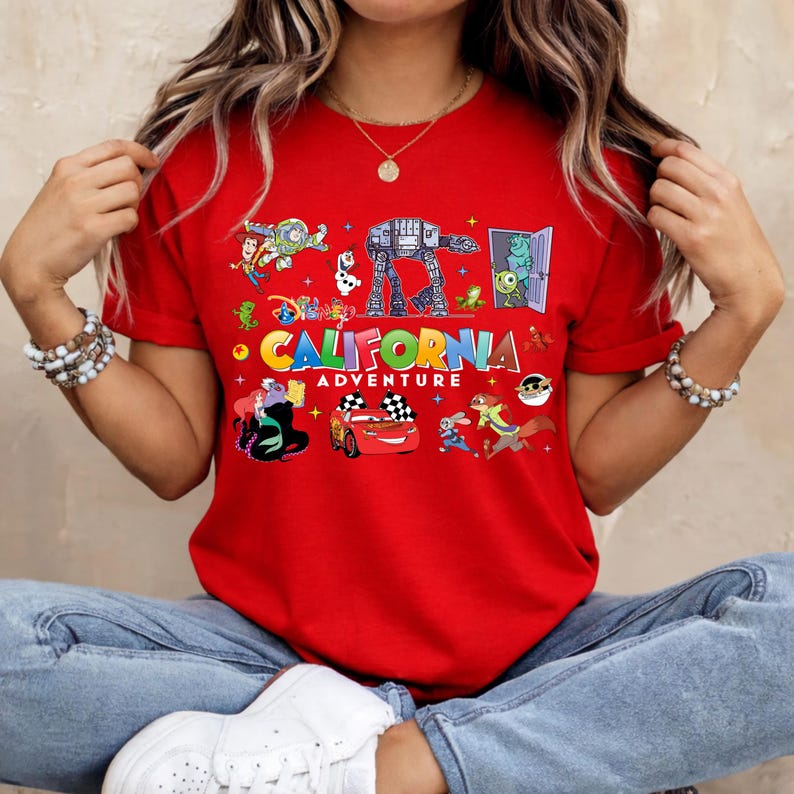 May include: Red t-shirt with a colorful graphic featuring various Disney characters and the words "CALIFORNIA ADVENTURE". The design includes images of a race car, an AT-AT walker, and other animated figures.