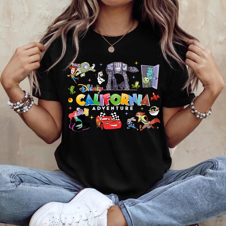 May include: Black t-shirt featuring colorful Disney characters and the text "California Adventure". The design includes characters from Toy Story, Monsters, Inc., Cars, and more. A fun and vibrant graphic tee.