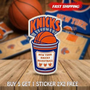 May include: A die-cut sticker featuring a blue and orange cup graphic with a basketball inside. The text reads KNICKS at the top and NEW YORK KNICKS BASKETBALL in the center, with three small basketball hoop icons at the bottom of the cup design.