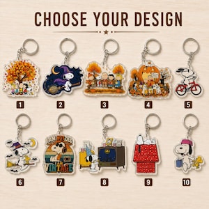 May include: Ten acrylic keychains featuring Peanuts characters in various scenes, including autumn themes, Halloween motifs, and retro designs. Each keychain has a metal ring and is numbered one through ten, with the text CHOOSE YOUR DESIGN above.
