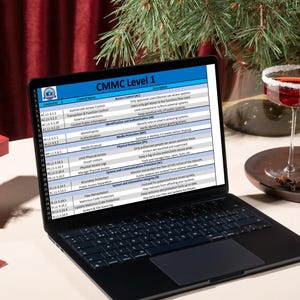 Könnte beinhalten: Ein schwarzer Laptop zeigt ein Dokument mit dem Titel "CMMC Level 1". Der Bildschirm zeigt eine Tabelle mit Textzeilen. Ein Cocktail mit gezuckertem Rand und ein Zweig Grünzeug befinden sich im Hintergrund.