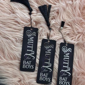 May include: Three black bookmarks with silver tassels. Each bookmark has the text "& Smutty for Bat Boys" printed in white.