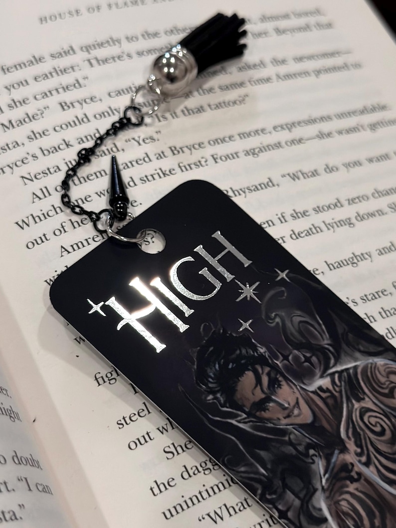 May include: A black bookmark with a silver chain and a black tassel. The bookmark features a silver metallic design that says "HIGH" with stars. The bookmark also features a black and white illustration of a man with a tattoo.