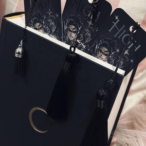 May include: Three black bookmarks with silver chains and black tassels. Each bookmark features a black and white illustration of a person with the word "High" printed on the bookmark.