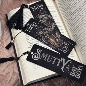 May include: Three black bookmarks with silver lettering. The bookmarks feature a dark fantasy illustration of a man with wings and a crown, the words "High Lord" and "Smutty for Bat Boys".
