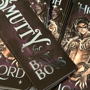 May include: A stack of dark brown bookmarks with silver foil lettering. The text on the bookmark reads "Smutty for Bad Boys" and "High Lord".