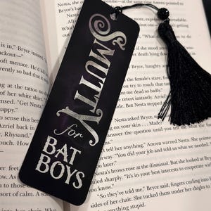 May include: A black bookmark with silver lettering that reads "Smutty for Bat Boys". The bookmark has a black tassel.