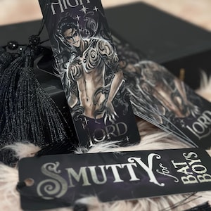 May include: A set of three black bookmarks with silver lettering. The bookmarks feature a shirtless man with tattoos, the words "High Lord", and the words "Smutty for Bad Boys".