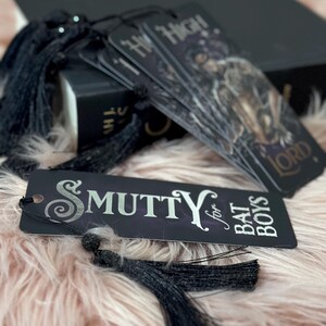 May include: Four black bookmarks with silver lettering and tassels. The bookmarks have the text "Hi Ho!" and "Smutty for Bat Boys".