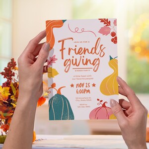 May include: A Friendsgiving dinner party invitation held by a person. The invitation features colorful illustrations of pumpkins and fall foliage. The text reads "Join us for a Friendsgiving Dinner Party" with the date and time of the event.