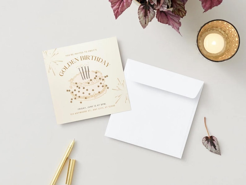 May include: A square invitation with the text "GOLDEN BIRTHDAY" and a cake illustration, accompanied by a white envelope and a gold pen. A lit candle in a gold holder and a small leaf are also present.