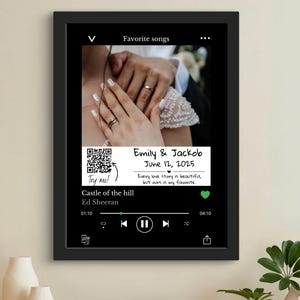 Könnte beinhalten: Schwarz gerahmter Druck mit Hochzeitsfoto und Musikplayer-Oberfläche. Der Druck zeigt die Namen "Emily & Jackob" und das Datum "12. Juni 2025". Der Song "Castle of the hill" von Ed Sheeran wird angezeigt.