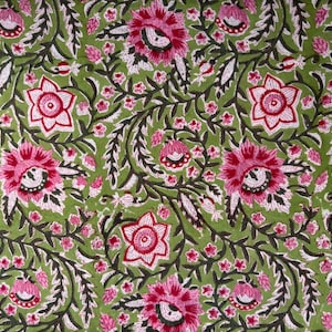 Op de afbeelding: Close-up van een stof met een bloemenpatroon. Het ontwerp toont grote roze bloemen met witte en rode details, kleine roze bloemen en donkergroene bladeren en wijnranken op een lichtgroene achtergrond. Het patroon herhaalt zich over de stof.