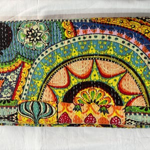 May include: A colorful, patterned textile with a vibrant design. The quilt features a mix of geometric and floral motifs in shades of blue, yellow, orange, and green. The stitching is visible, adding texture to the overall design.