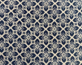 Pode incluir: Padrão repetitivo de motivos florais em azul marinho e creme. As flores têm cinco pétalas e estão dispostas em uma grade. O fundo é bege claro, criando contraste com as flores azul escuras.
