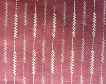 May include: Close-up of a fabric with a repeating pattern of white arrow-like shapes on a dusty rose background. The arrows are arranged in vertical lines, creating a textured design.