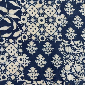 May include: A patchwork textile with a repeating pattern of white floral and geometric designs on a dark blue background. The fabric is divided into rectangular sections, each showcasing a different variation of the pattern. The design evokes block printing.