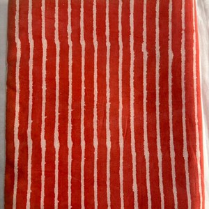 May include: Folded fabric with a vibrant red background and vertical white stripes. The stripes have a slightly irregular, hand-drawn appearance, creating a textured look. The fabric is likely cotton or a similar material.