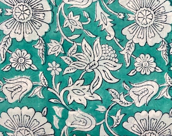May include: Close-up of a teal fabric with a white floral pattern. The design features large, stylized flowers, smaller blossoms, and intricate leaf and vine details. The print has a block-print style.