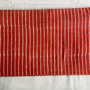 May include: Folded fabric with a repeating pattern of vertical white stripes on a red background. The fabric is folded and appears to be made of a soft material. The stripes are evenly spaced.