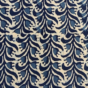 Op de afbeelding: Close-up van een stof met een herhalend patroon van donkerblauwe en lichtblauwe bloemvormen op een crèmekleurige achtergrond. Het ontwerp heeft een vloeiend, organisch gevoel, dat lijkt op gestileerde bladeren of water.