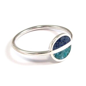 May include: A silver ring with a blue and green stone set in a circle.