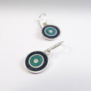 May include: A pair of silver earrings with a blue and green stone inlay in the shape of an eye. The earrings have a simple hook design.