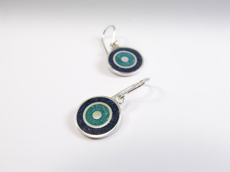 May include: A pair of silver earrings with a blue and green stone inlay in the shape of an eye. The earrings have a simple hook design.