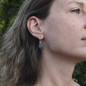 May include: A woman wearing a pair of silver earrings with a blue and green oval-shaped stone.