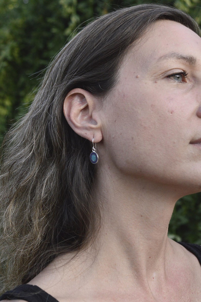 May include: A woman wearing a pair of silver earrings with a blue and green oval-shaped stone.