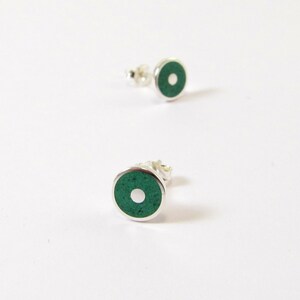 May include: A pair of silver stud earrings with a green circle and a white dot in the center.