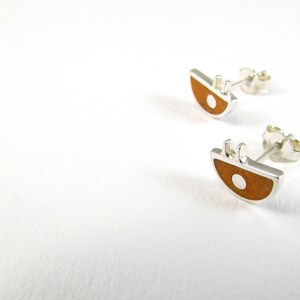 May include: A pair of silver stud earrings with a brown and white geometric design. The earrings are shaped like a half-circle with a small white circle in the center.