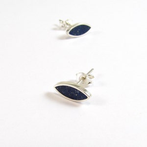 May include: A pair of silver stud earrings with a dark blue oval-shaped stone.