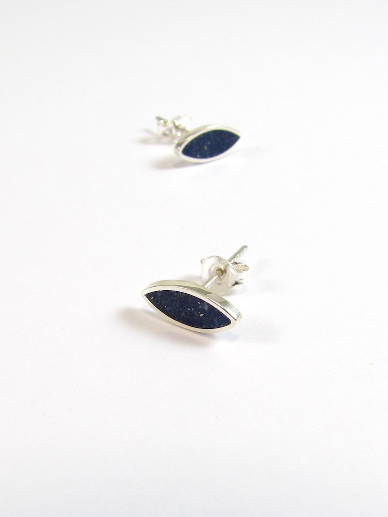 May include: A pair of silver stud earrings with a dark blue oval-shaped stone.