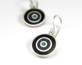 Puede incluir: Un par de pendientes de plata con un diseño circular negro y azul. El centro del círculo tiene una pequeña piedra turquesa.