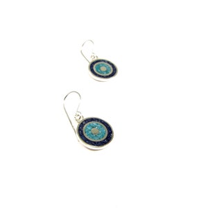 May include: A pair of silver earrings with blue and turquoise stone inlays, shaped like an eye. The earrings have a simple hook design.