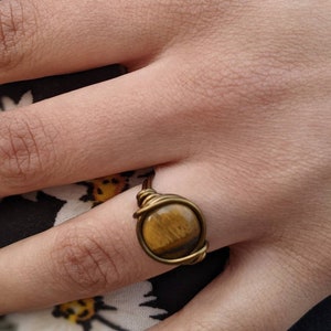 May include: A gold wire wrapped ring with a round tiger's eye gemstone.
