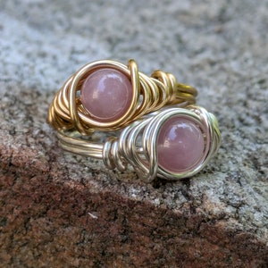 May include: Two wire-wrapped rings with pink gemstone accents. The rings are made with gold and silver wire.