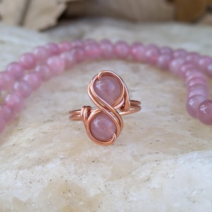 May include: A rose quartz ring with two stones wrapped in copper wire, forming an infinity symbol.