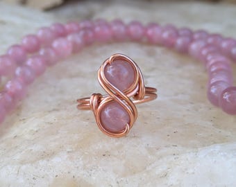May include: A rose quartz ring with two stones wrapped in copper wire, forming an infinity symbol.