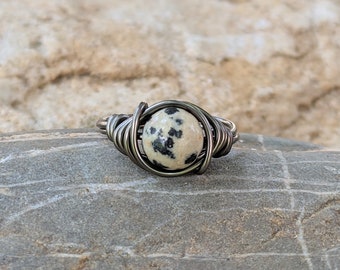 May include: A silver wire wrapped ring with a white and black dalmatian jasper stone.
