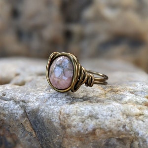 Puede incluir: Un anillo de piedra preciosa rosa y gris con engaste de alambre de lat&oacute;n.