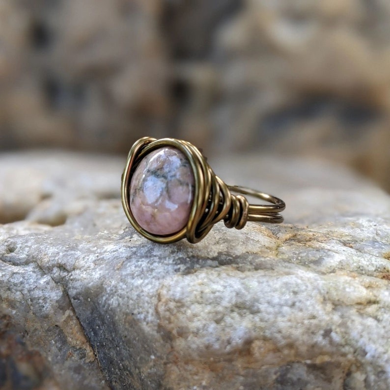 Puede incluir: Un anillo de piedra preciosa rosa y gris con engaste de alambre de lat&oacute;n.