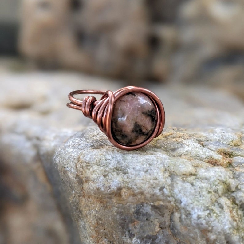 May include: A copper wire wrapped ring with a pink and black gemstone.